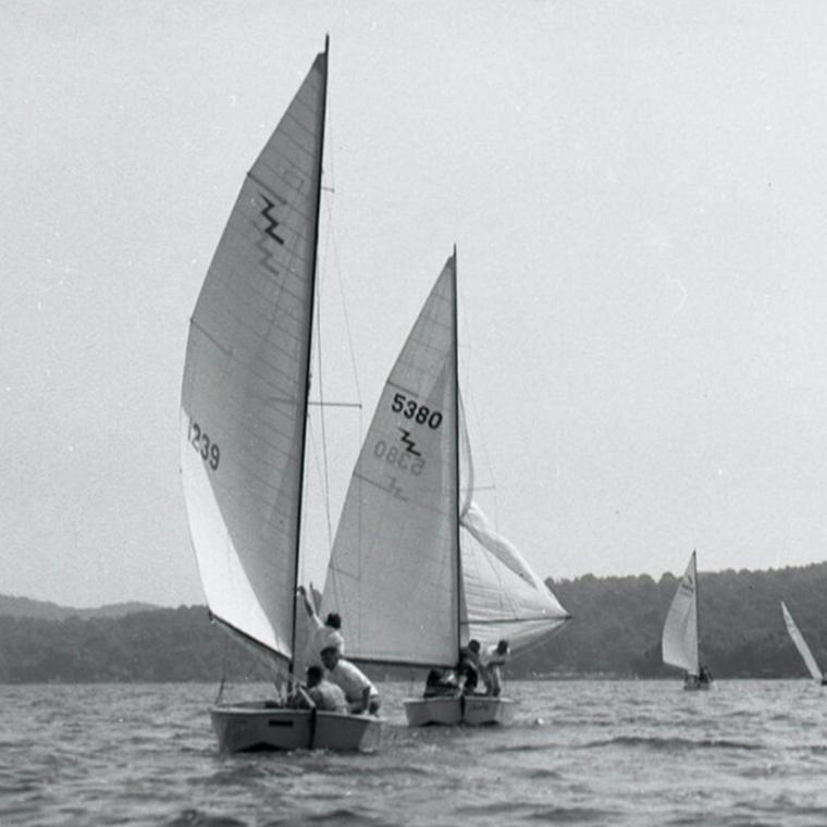 Two dinghies under full sail in black and white.