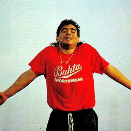 A footballer in a red sportswear tee, arms spread wide.