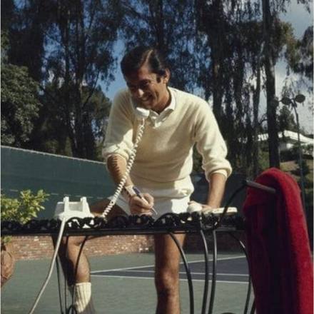 A player stringing a racket beside a clay court.