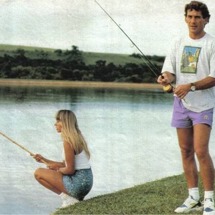 Two people fishing from a grassy riverbank.