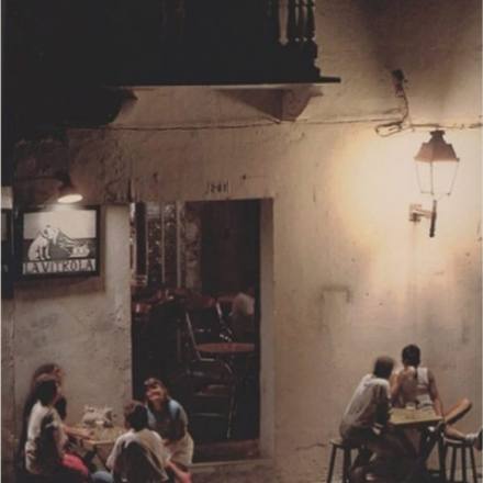 People gathered at tables outside a lit café at night.